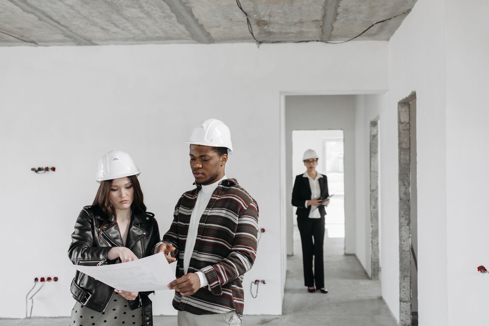 Contractor and client in hard hats reviewing building plans in an unfinished house