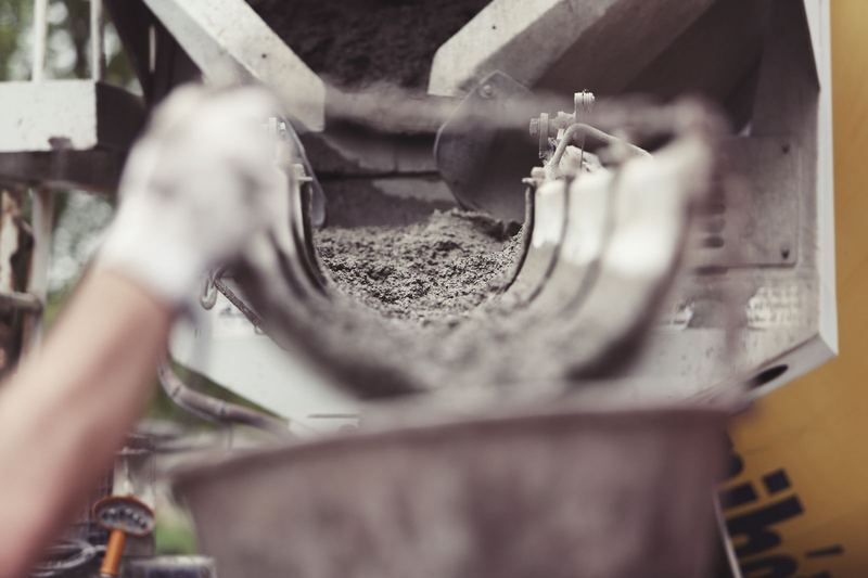 Close-up of concrete being poured from a mixer truck at a construction site with a worker's hand visible