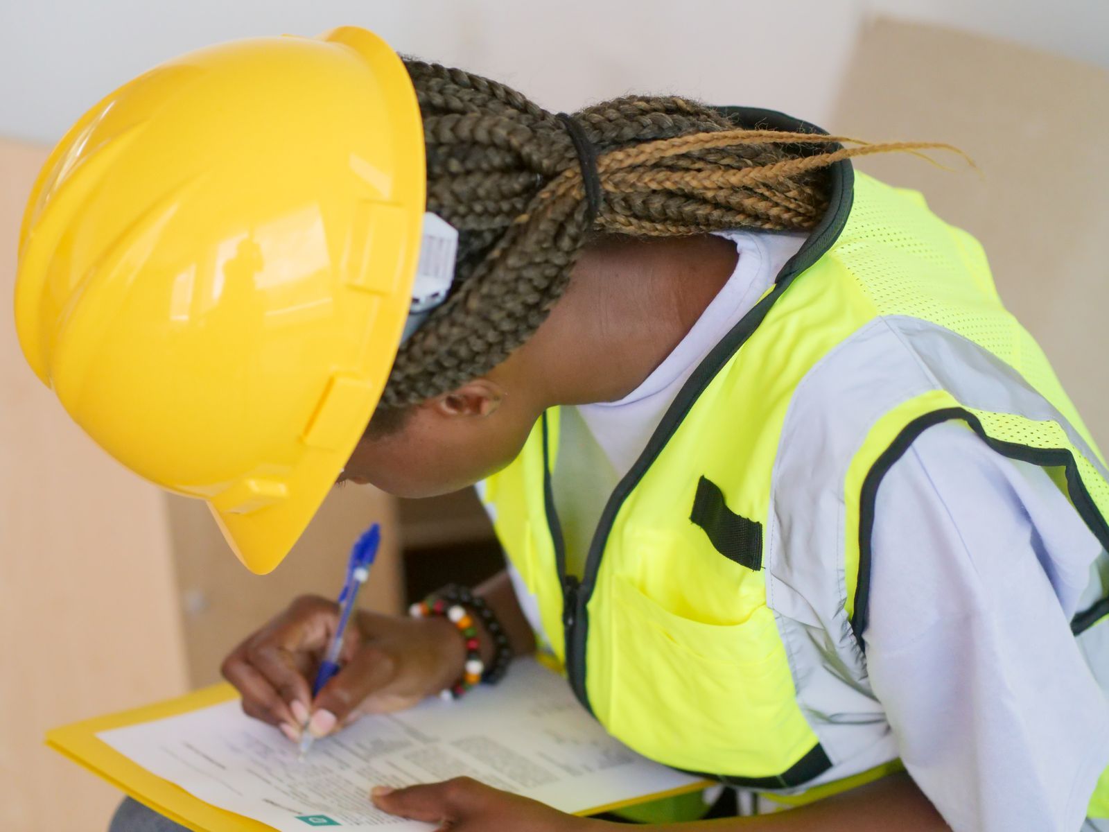 A female engineer in PPE writing on a clipboard at a construction site