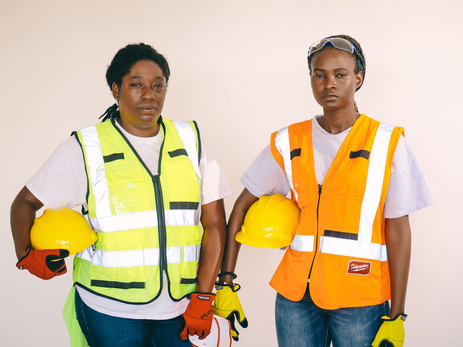 Two women construction workers wearing safety vests and holding hard hats