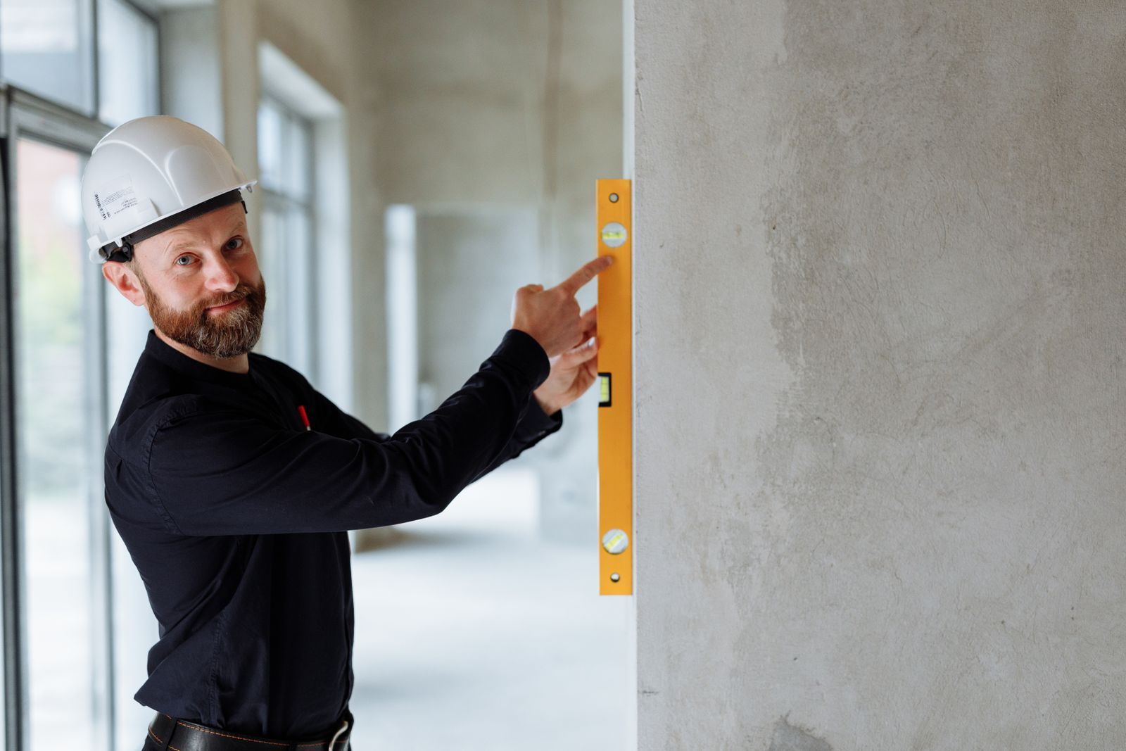 Engineer with hard hat using a spirit level on a wall at a construction site