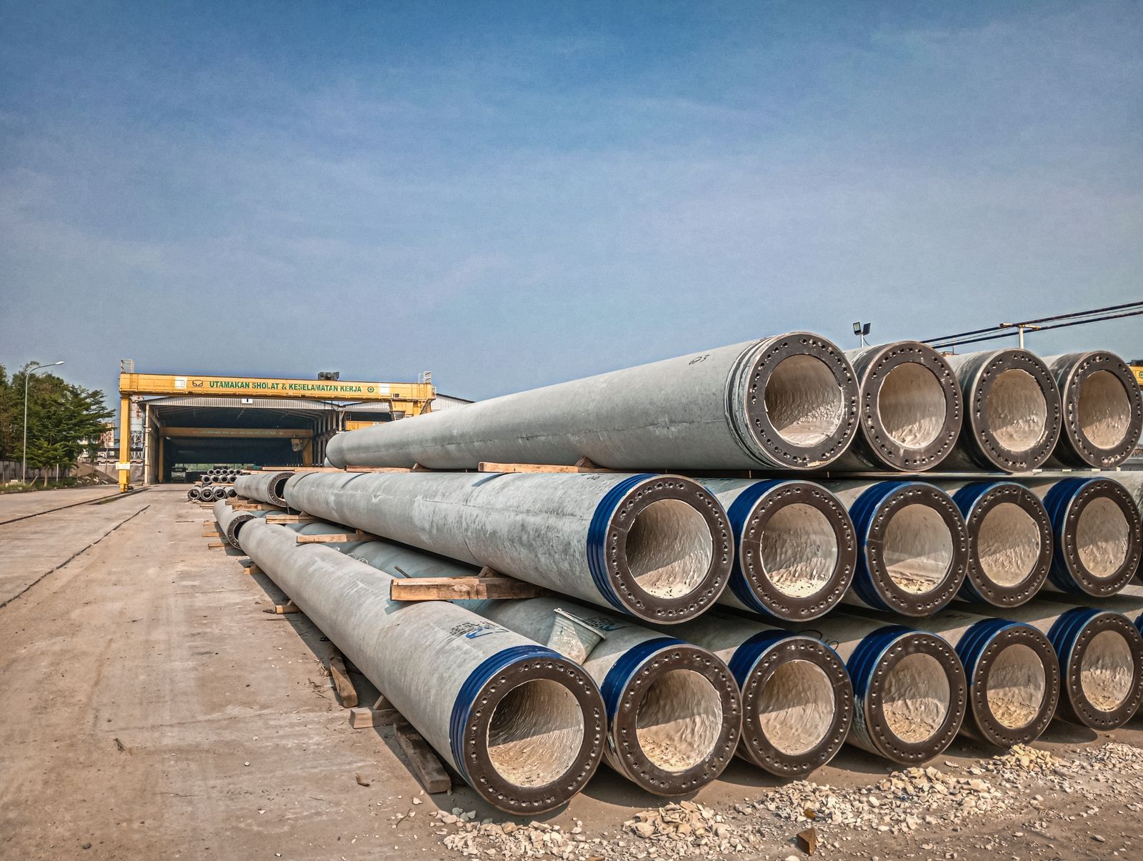 Stacked industrial concrete pipes near a construction area under clear skies