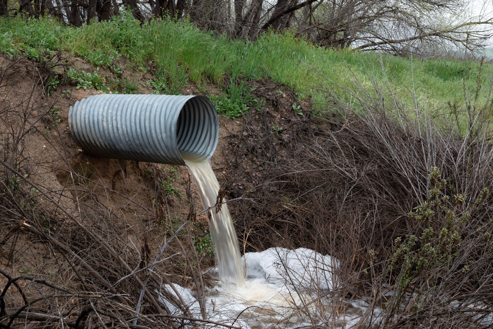 A rural drainage pipe pouring water into a natural ravine, surrounded by green vegetation