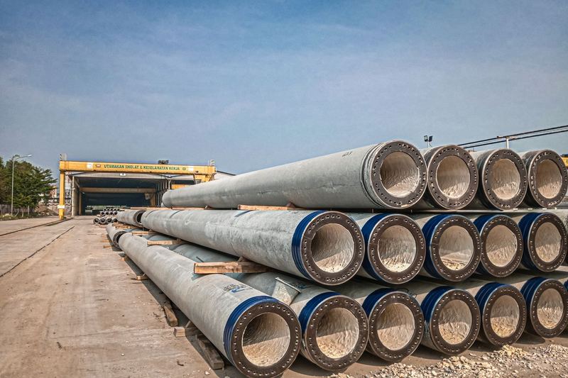 Stacked industrial concrete pipes near a construction area under clear skies