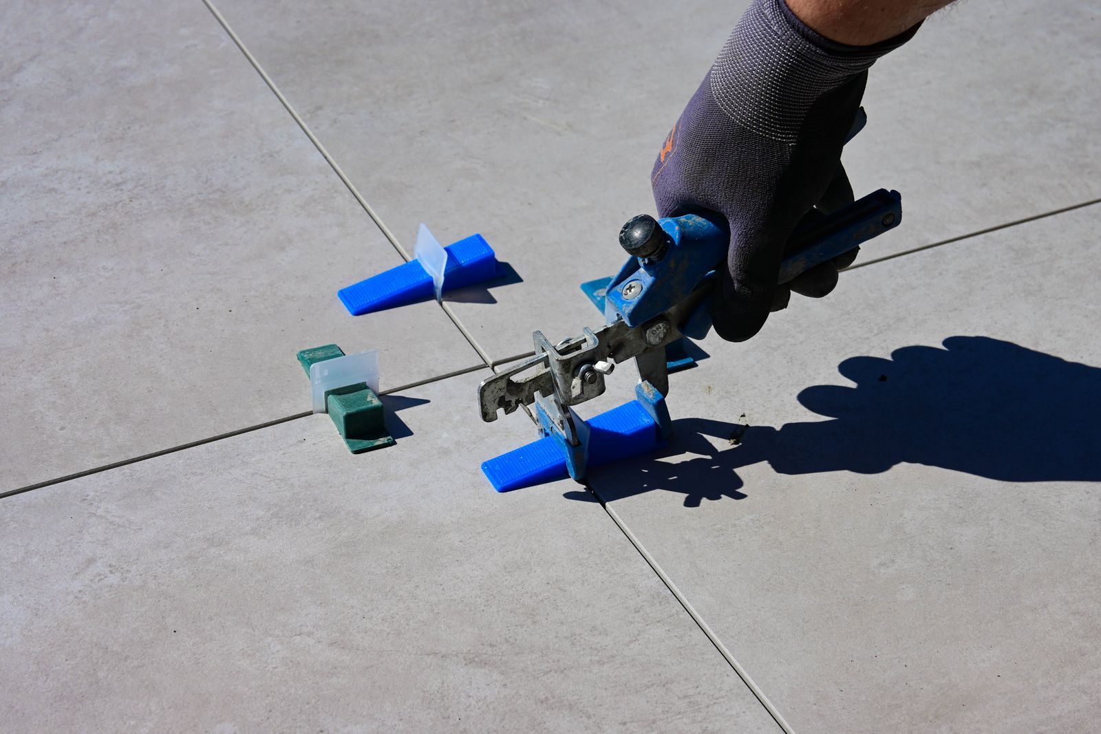 A gloved hand using a leveling tool to install tiles with spacers