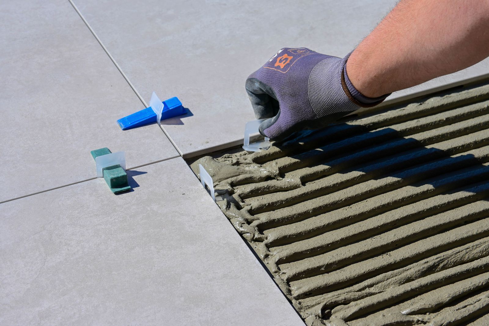 Gloved hand laying floor tiles with levelling clips