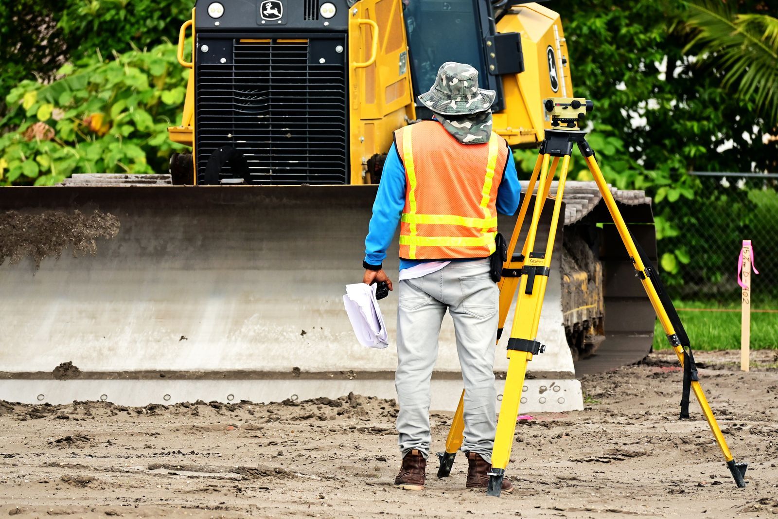 Surveyor with equipment at an active construction site, observing bulldozer operations
