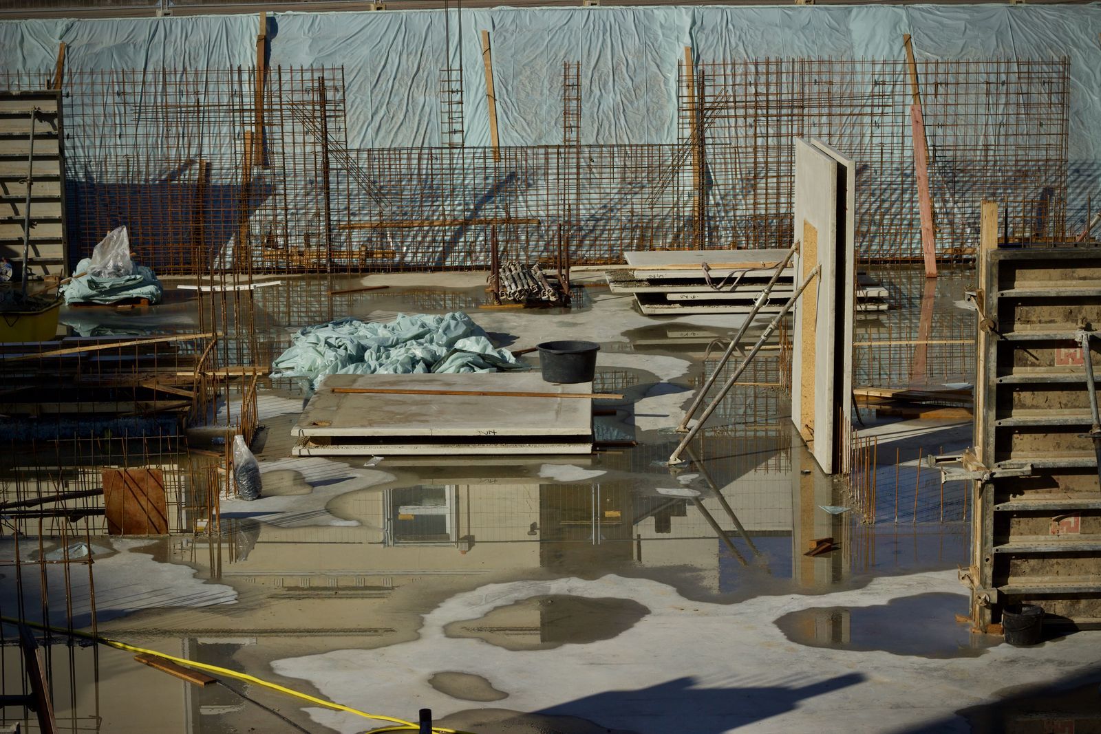 A flooded construction site with scattered materials and visible metal reinforcement