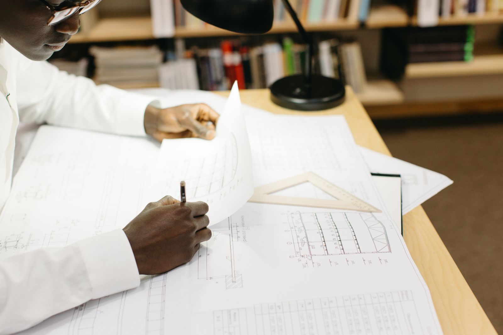 Black male architect working on blueprints at a desk in a well-lit office