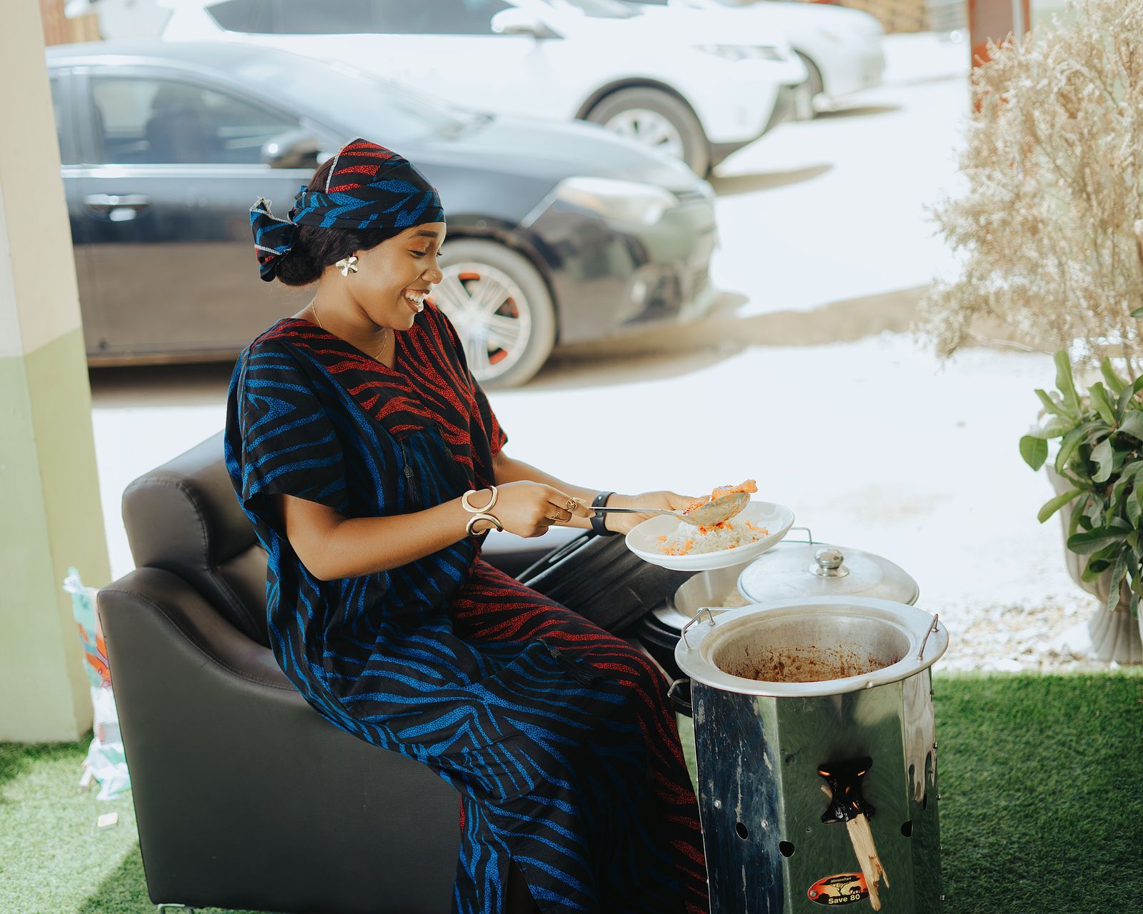 Smiling African woman cooking a traditional meal outdoors, serving food from a pot