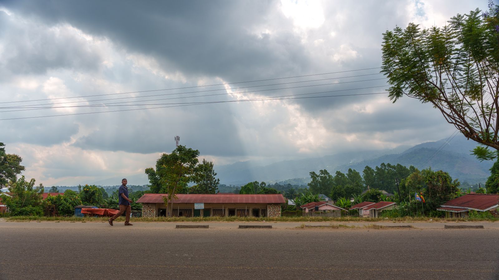 Houses along a rural road in Uganda under a cloudy sky