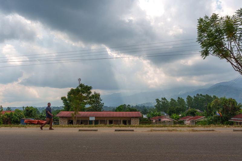Houses along a rural road in Uganda under a cloudy sky