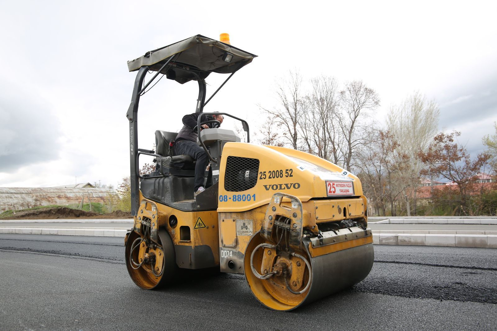 A road roller compacting fresh asphalt on a new roadway with a construction worker operating the vehicle