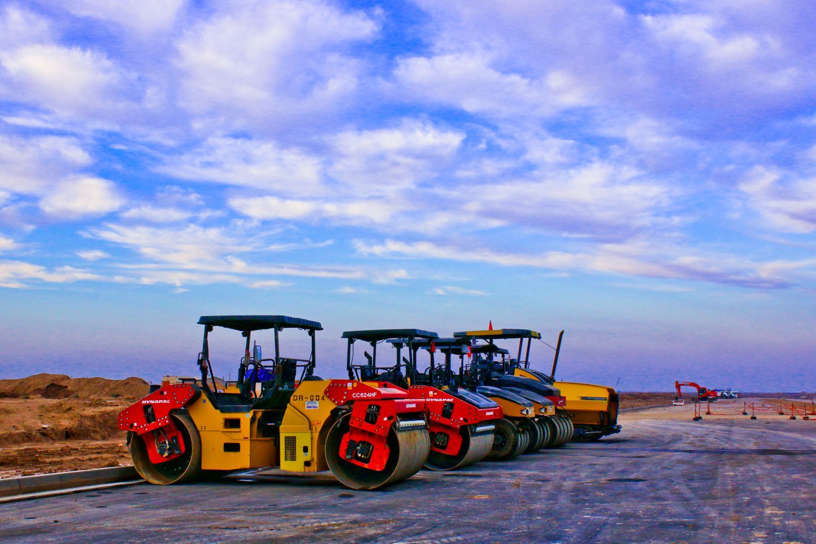 Road rollers parked on a construction site under a bright blue sky