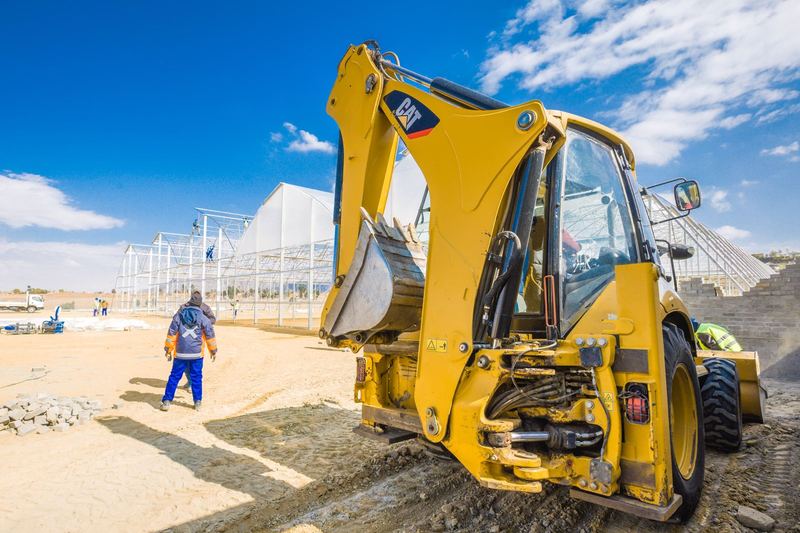 Construction scene with yellow excavator and workers under a clear blue sky in South Africa