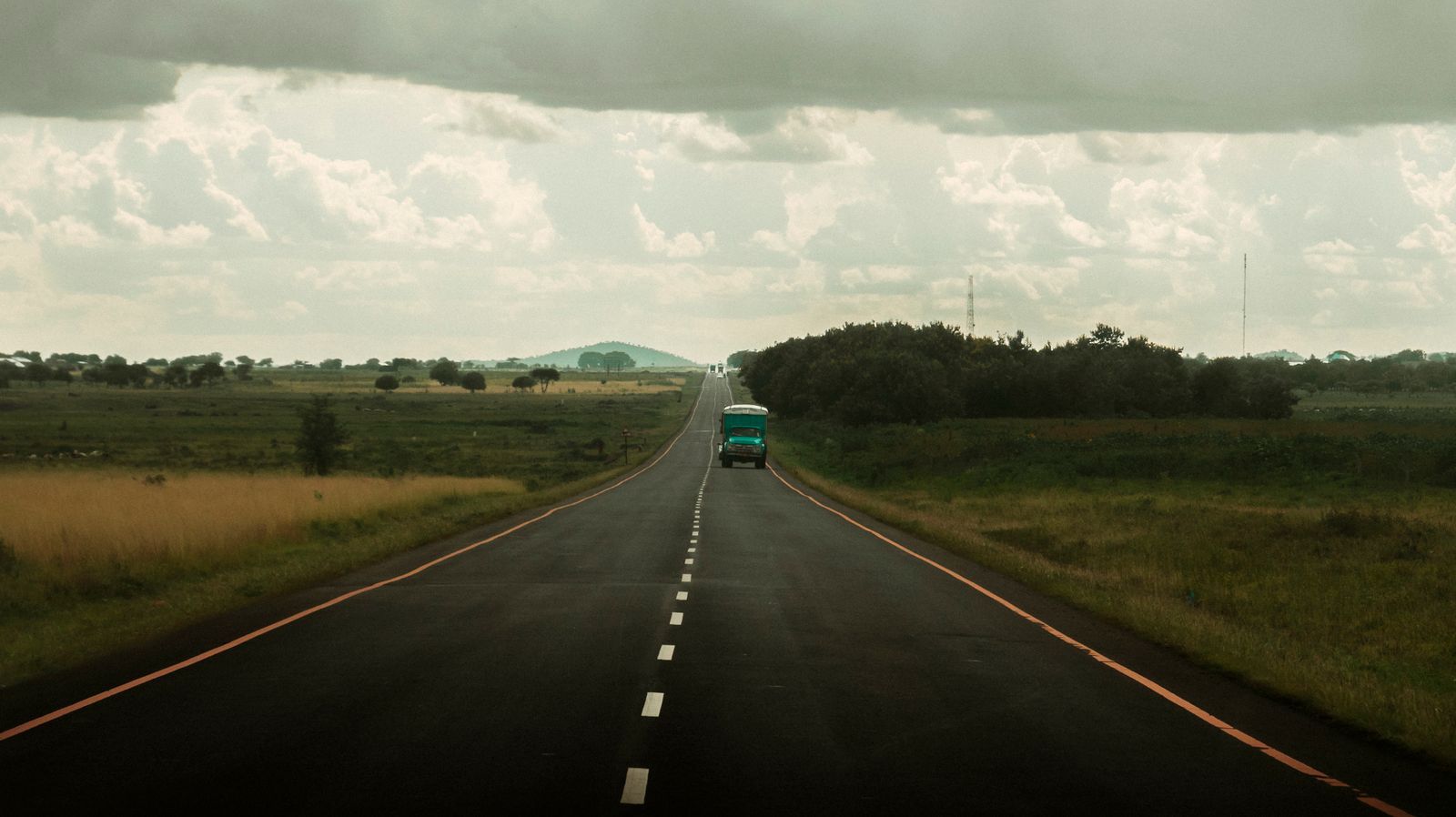 An open road in Tanzania with a lone truck under a cloudy sky